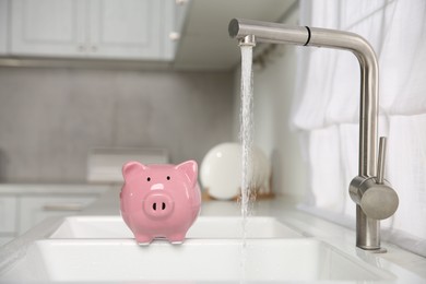 Water saving concept. Piggy bank and stream of water flowing from tap in kitchen