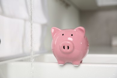 Photo of Water saving concept. Piggy bank and stream of water in kitchen