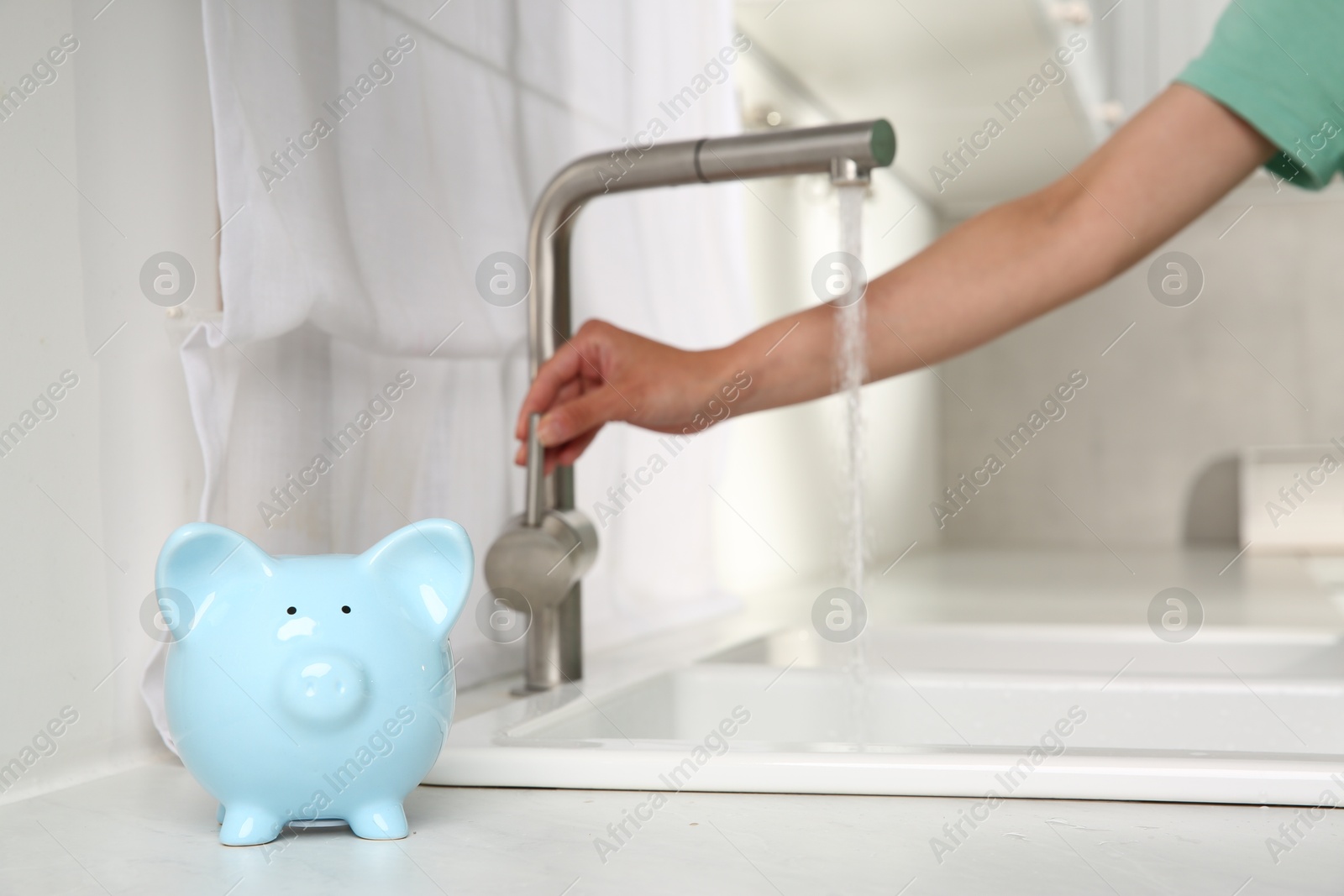 Water saving concept. Woman checking water flow in kitchen, focus on piggy bank Photo of Water saving concept. Woman checking water flow in kitchen, focus on piggy bank