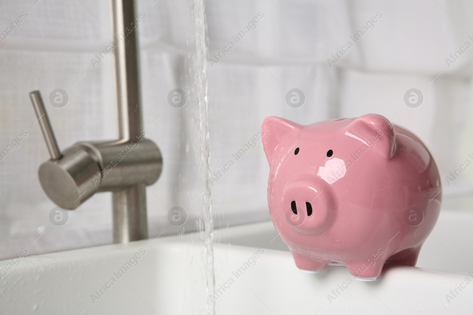 Water saving concept. Piggy bank and stream of water flowing from tap in kitchen Photo of Water saving concept. Piggy bank and stream of water flowing from tap in kitchen