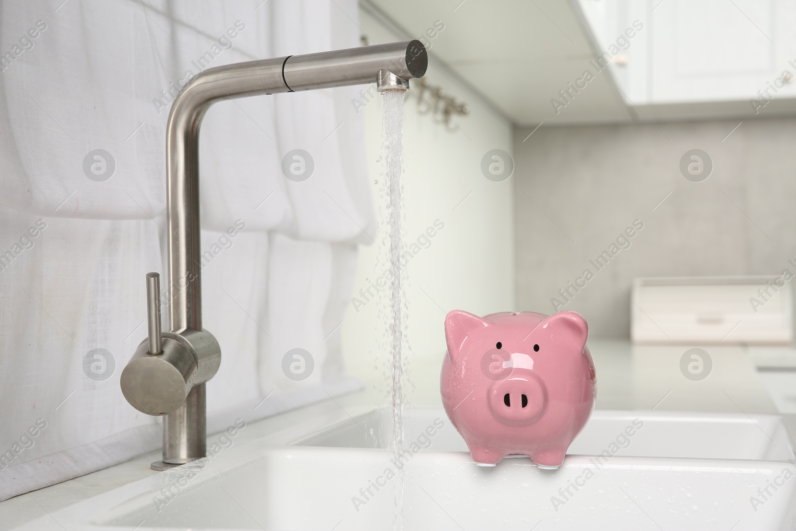 Photo of Water saving concept. Piggy bank and stream of water flowing from tap in kitchen