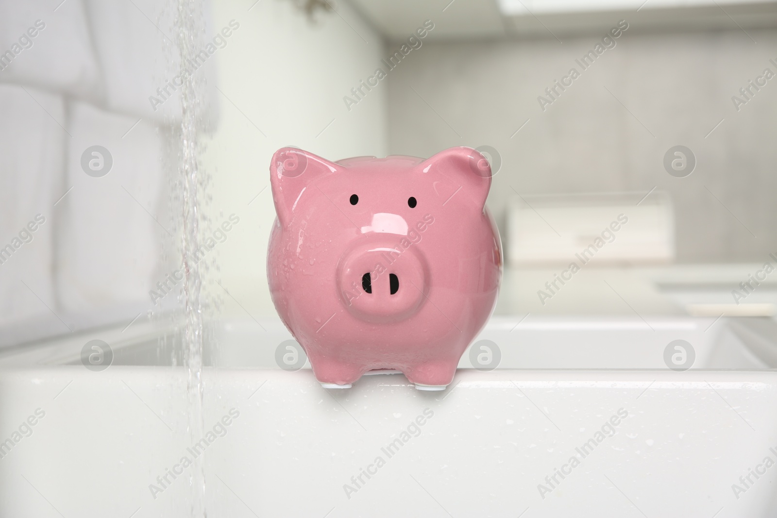 Water saving concept. Piggy bank and stream of water in kitchen Photo of Water saving concept. Piggy bank and stream of water in kitchen