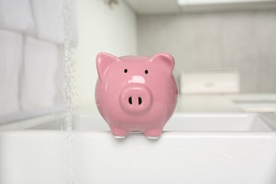 Photo of Water saving concept. Piggy bank and stream of water in kitchen