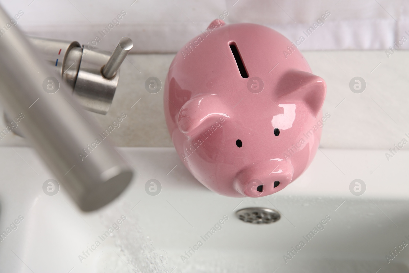 Photo of Water saving concept. Piggy bank and stream of water flowing from tap in kitchen, above view