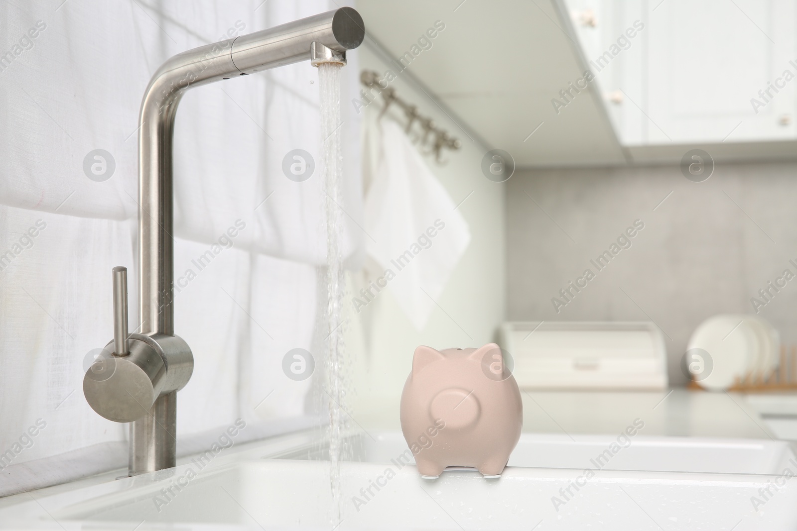 Photo of Water saving concept. Piggy bank and stream of water flowing from tap in kitchen