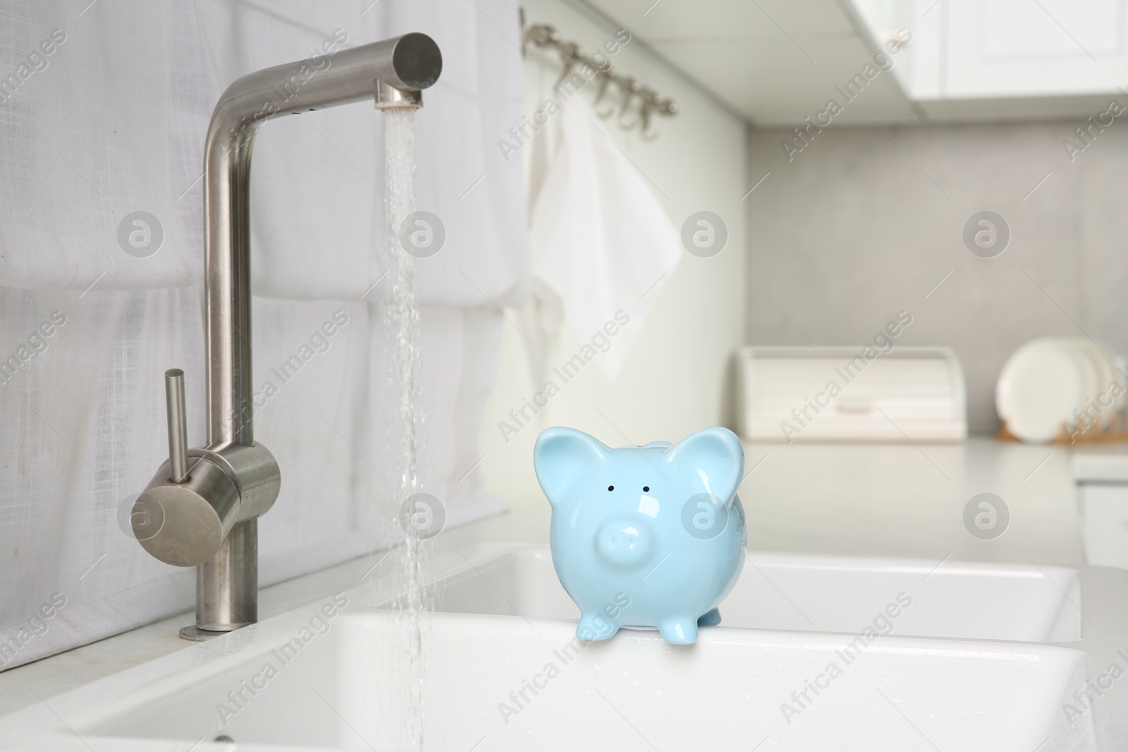 Photo of Water saving concept. Piggy bank and stream of water flowing from tap in kitchen