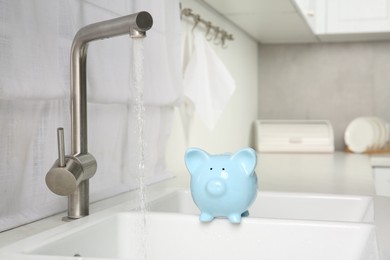 Photo of Water saving concept. Piggy bank and stream of water flowing from tap in kitchen