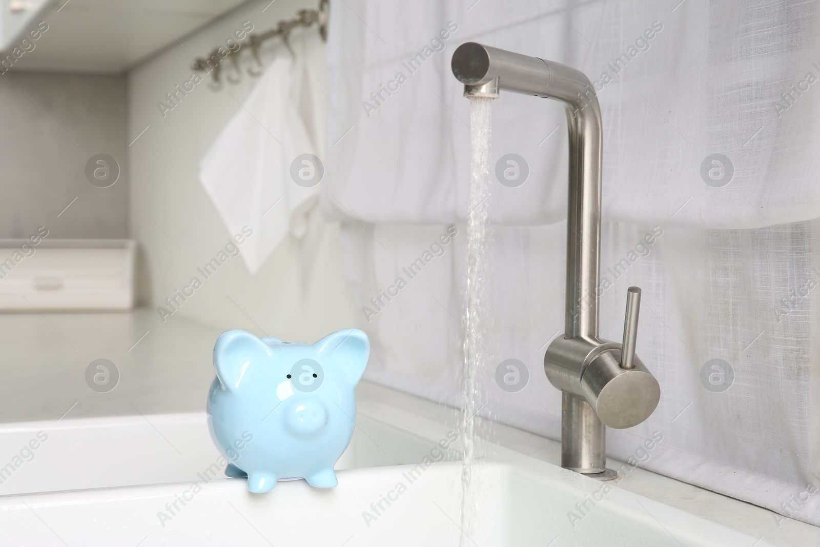 Photo of Water saving concept. Piggy bank and stream of water flowing from tap in kitchen