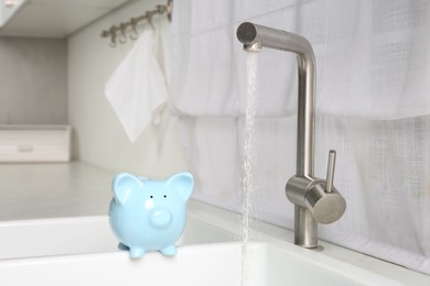 Photo of Water saving concept. Piggy bank and stream of water flowing from tap in kitchen