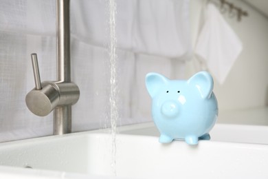 Photo of Water saving concept. Piggy bank and stream of water flowing from tap in kitchen