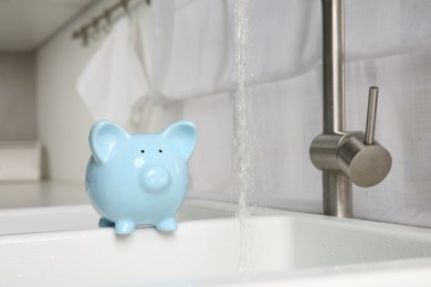 Photo of Water saving concept. Piggy bank and stream of water flowing from tap in kitchen