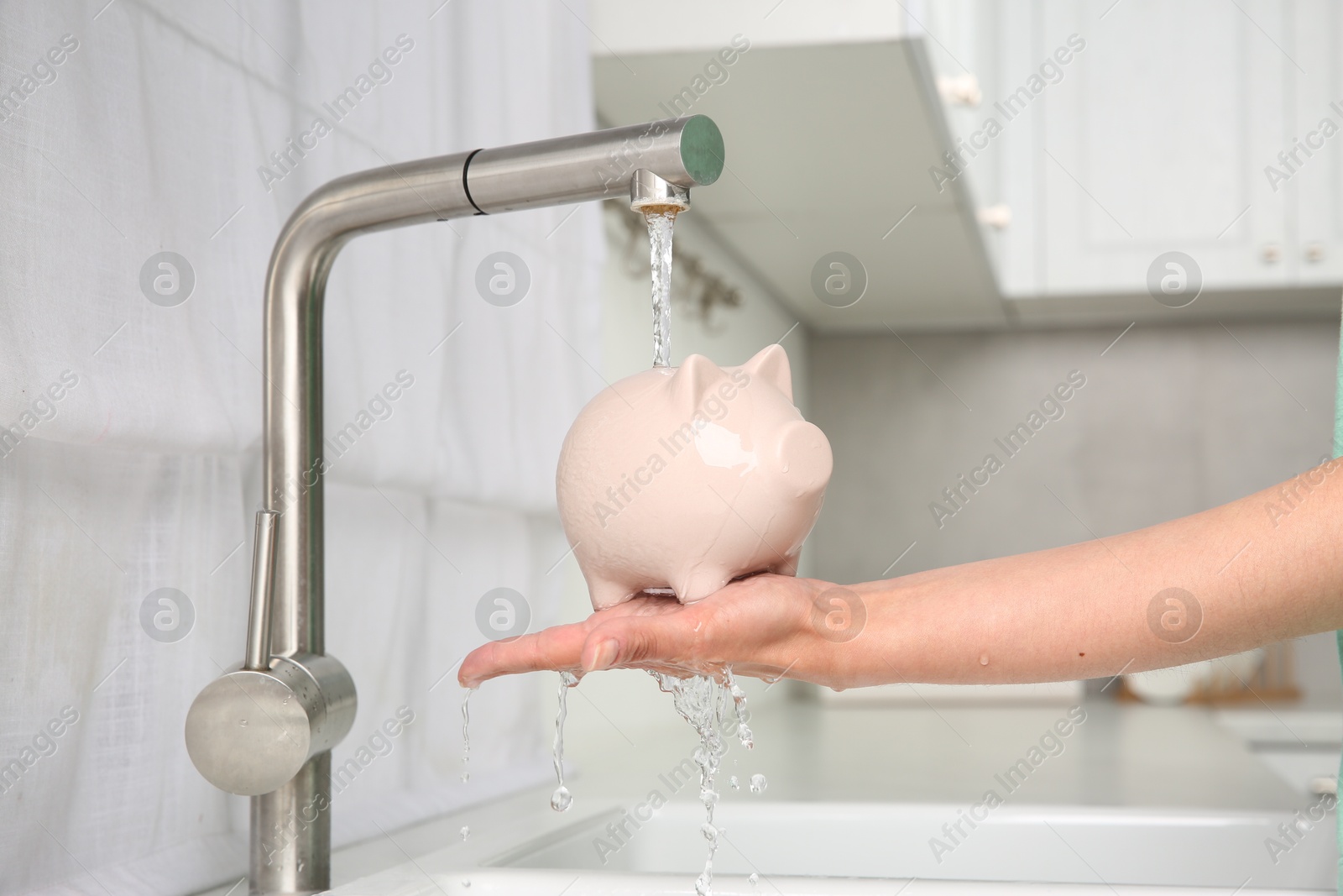 Photo of Water saving concept. Woman with piggy bank under tap water in kitchen