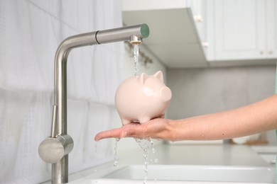 Photo of Water saving concept. Woman with piggy bank under tap water in kitchen