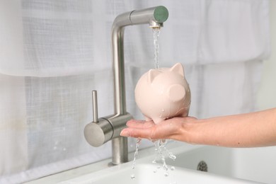 Photo of Water saving concept. Woman with piggy bank under tap water in kitchen