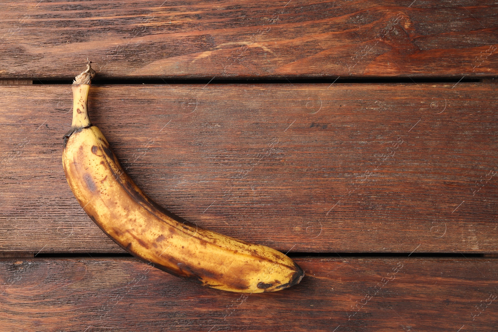 Photo of Overripe banana with dark spots on white wooden table, top view. Space for text