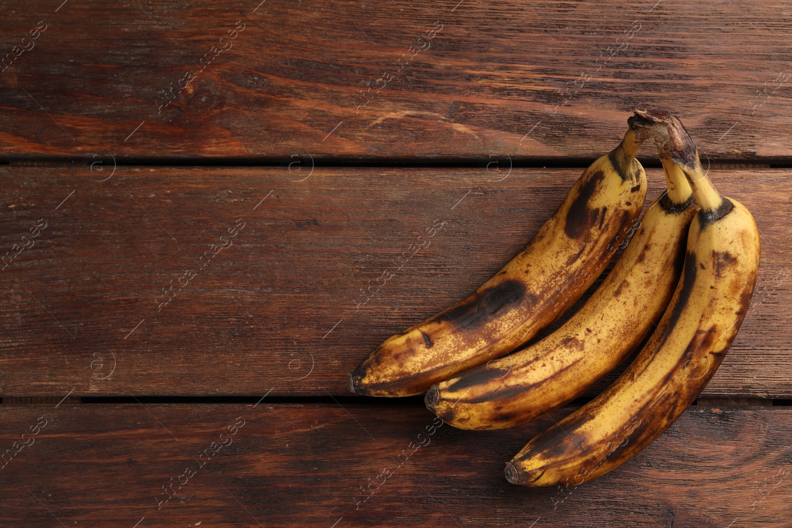 Photo of Bunch of ripe bananas with dark spots on wooden table, top view. Space for text