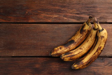 Photo of Bunch of ripe bananas with dark spots on wooden table, top view. Space for text