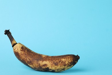 Overripe banana with dark spots on light blue background. Space for text