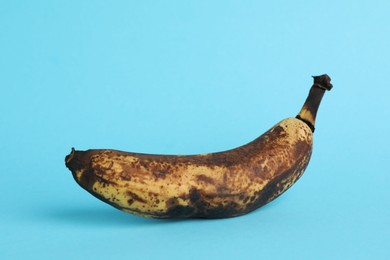 Photo of Overripe banana with dark spots on light blue background, closeup