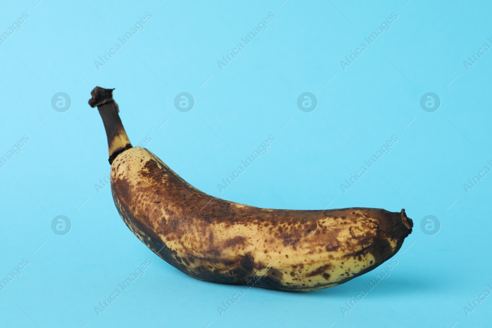 Photo of Overripe banana with dark spots on light blue background, closeup