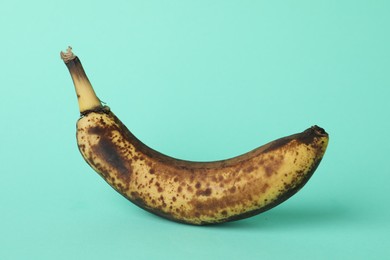 Photo of Overripe banana with dark spots on turquoise background, closeup