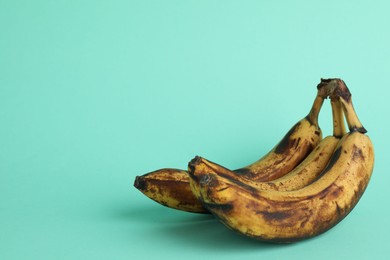 Photo of Overripe bananas with dark spots on turquoise background, closeup. Space for text