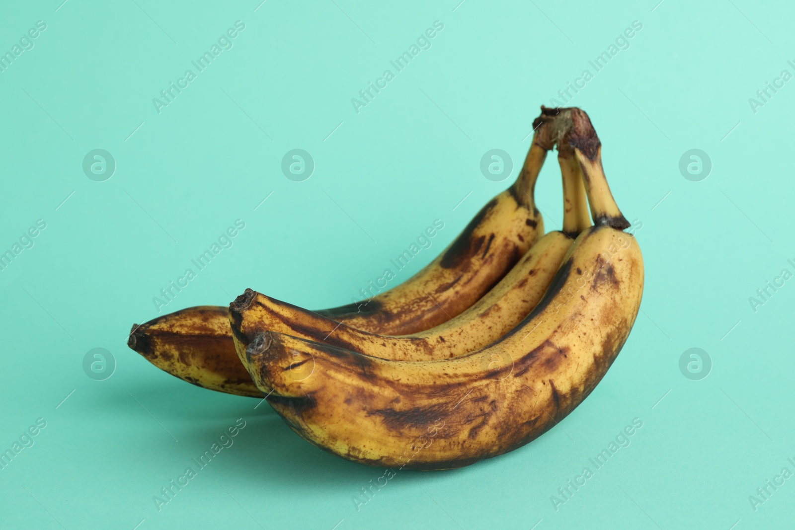 Photo of Overripe bananas with dark spots on turquoise background, closeup