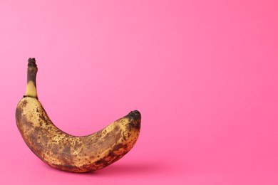 Photo of Overripe banana with dark spots on pink background. Space for text