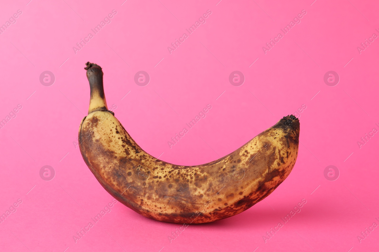 Photo of Overripe banana with dark spots on pink background