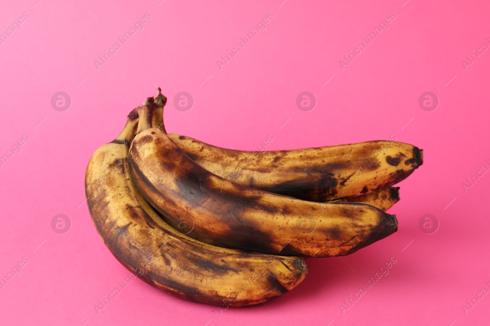 Photo of Bunch of ripe bananas with dark spots on pink background