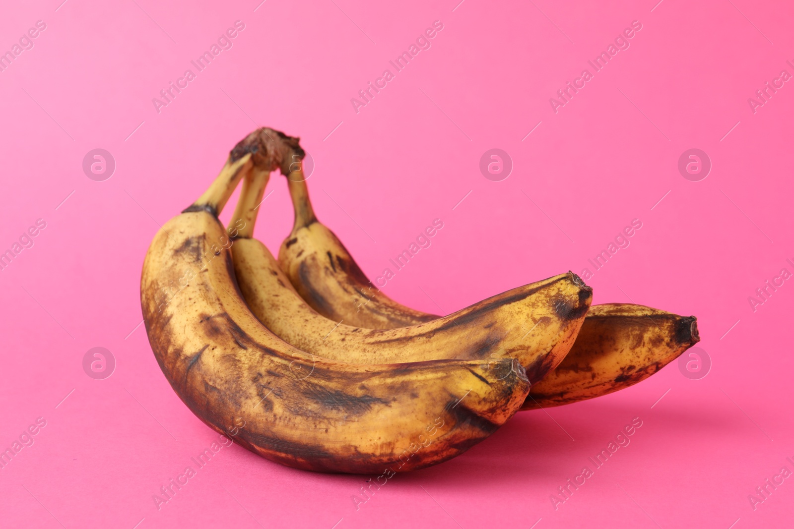 Photo of Bunch of ripe bananas with dark spots on pink background, closeup