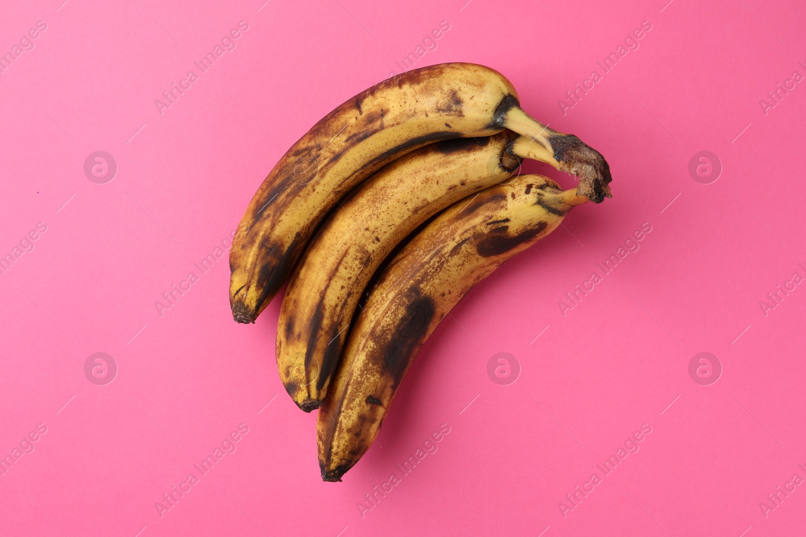 Photo of Bunch of ripe bananas with dark spots on pink background, top view