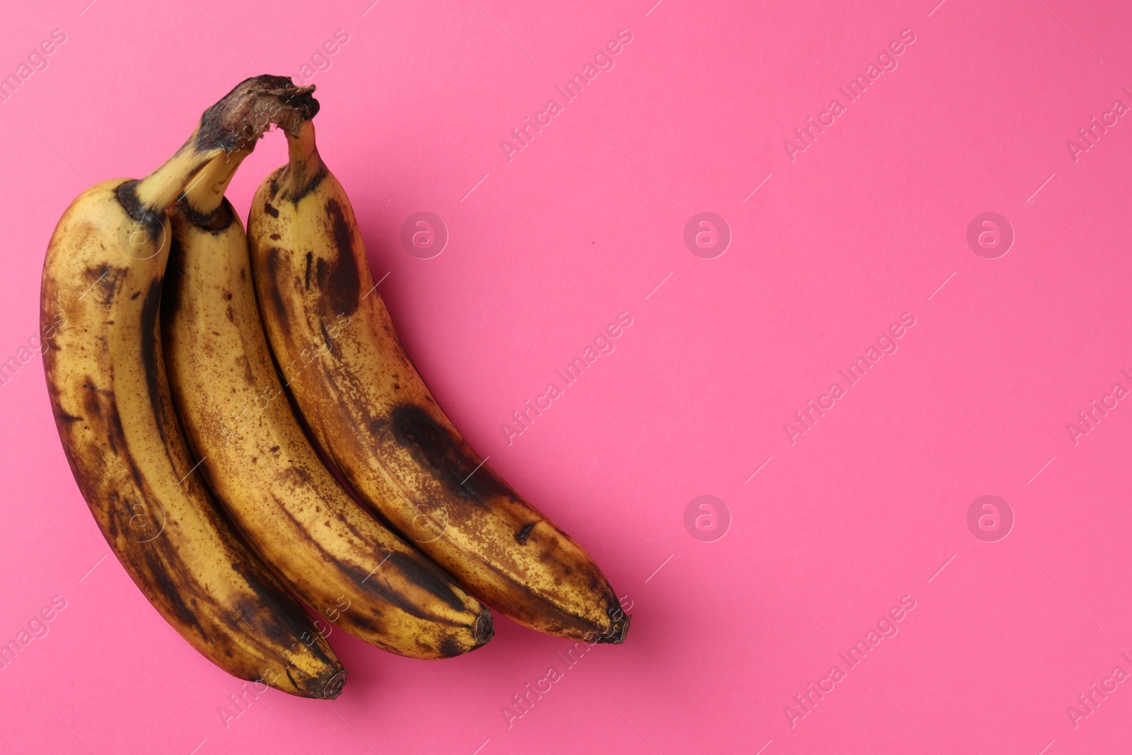 Photo of Bunch of ripe bananas with dark spots on pink background, top view. Space for text