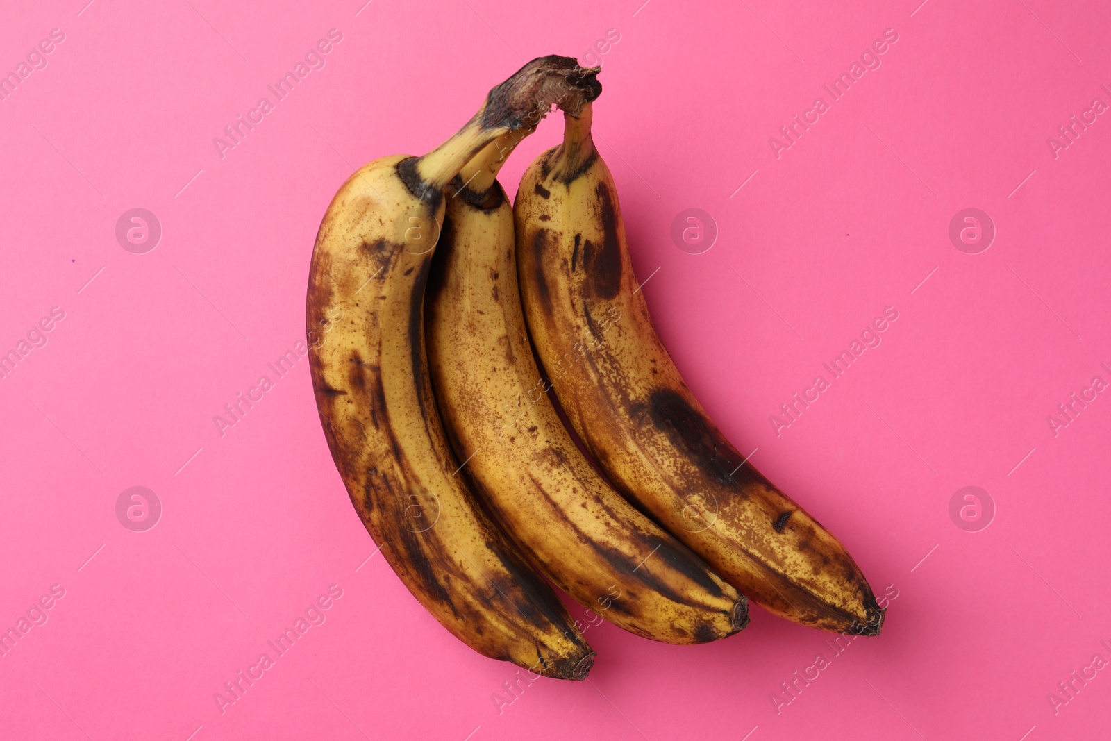 Photo of Bunch of ripe bananas with dark spots on pink background, top view