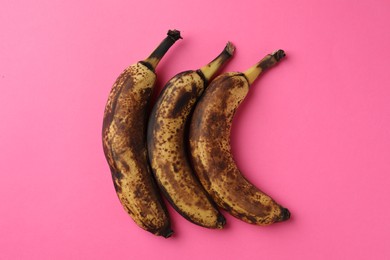 Overripe bananas with dark spots on pink background, top view