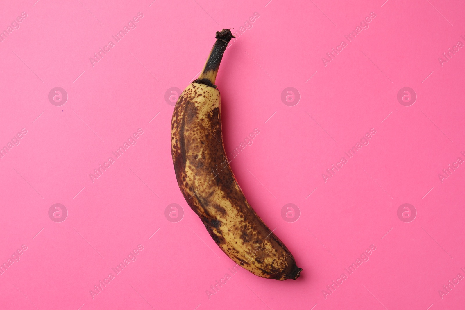 Photo of Overripe banana with dark spots on pink background, top view