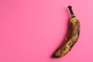 Overripe banana with dark spots on pink background, top view. Space for text