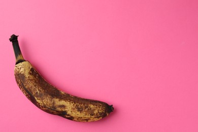 Overripe banana with dark spots on pink background, top view. Space for text