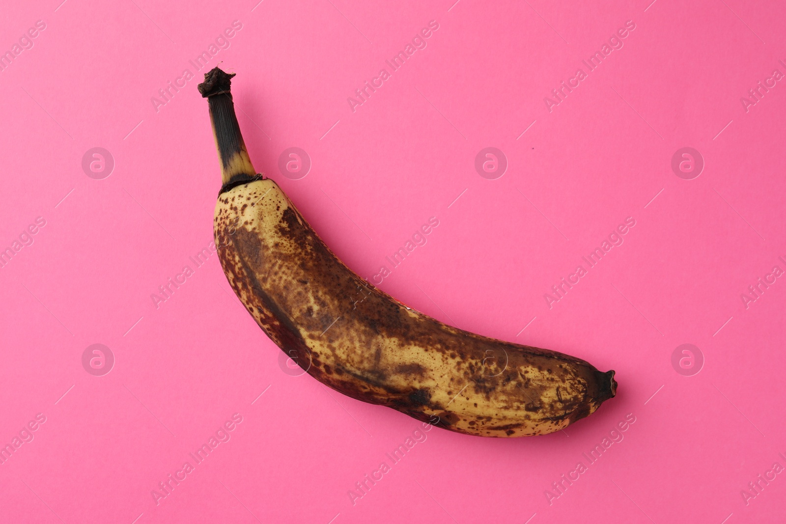 Photo of Overripe banana with dark spots on pink background, top view