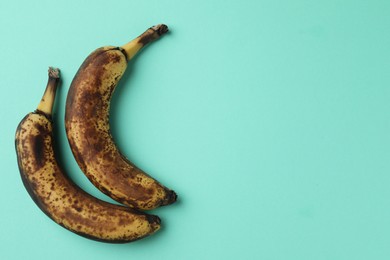 Overripe bananas with dark spots on turquoise background, top view. Space for text