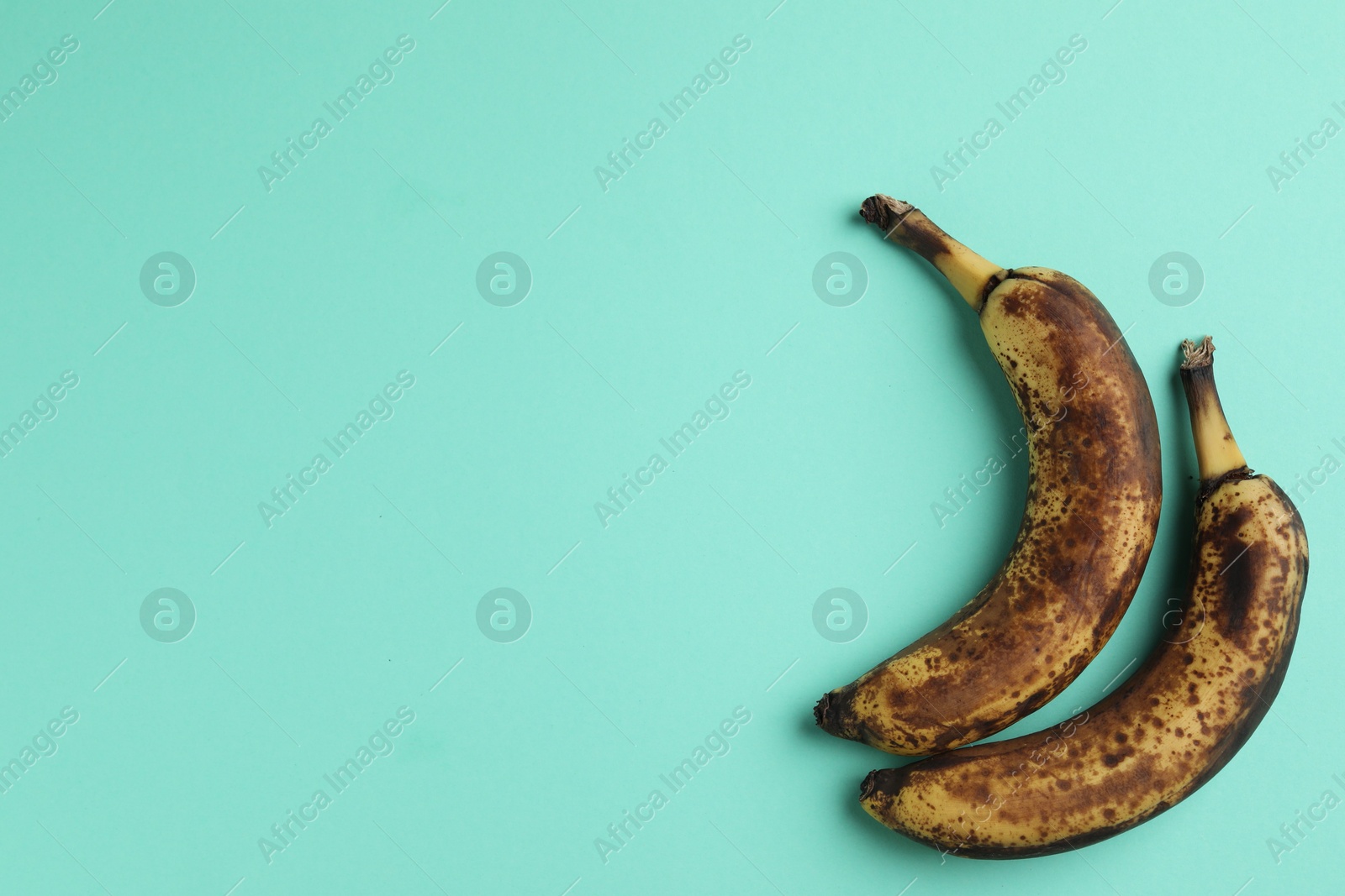 Photo of Overripe bananas with dark spots on turquoise background, top view. Space for text