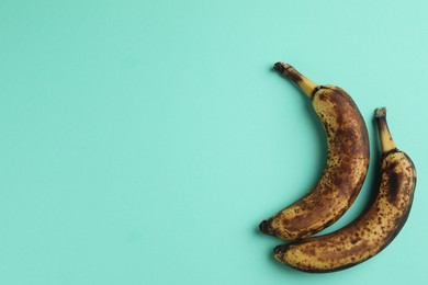 Photo of Overripe bananas with dark spots on turquoise background, top view. Space for text