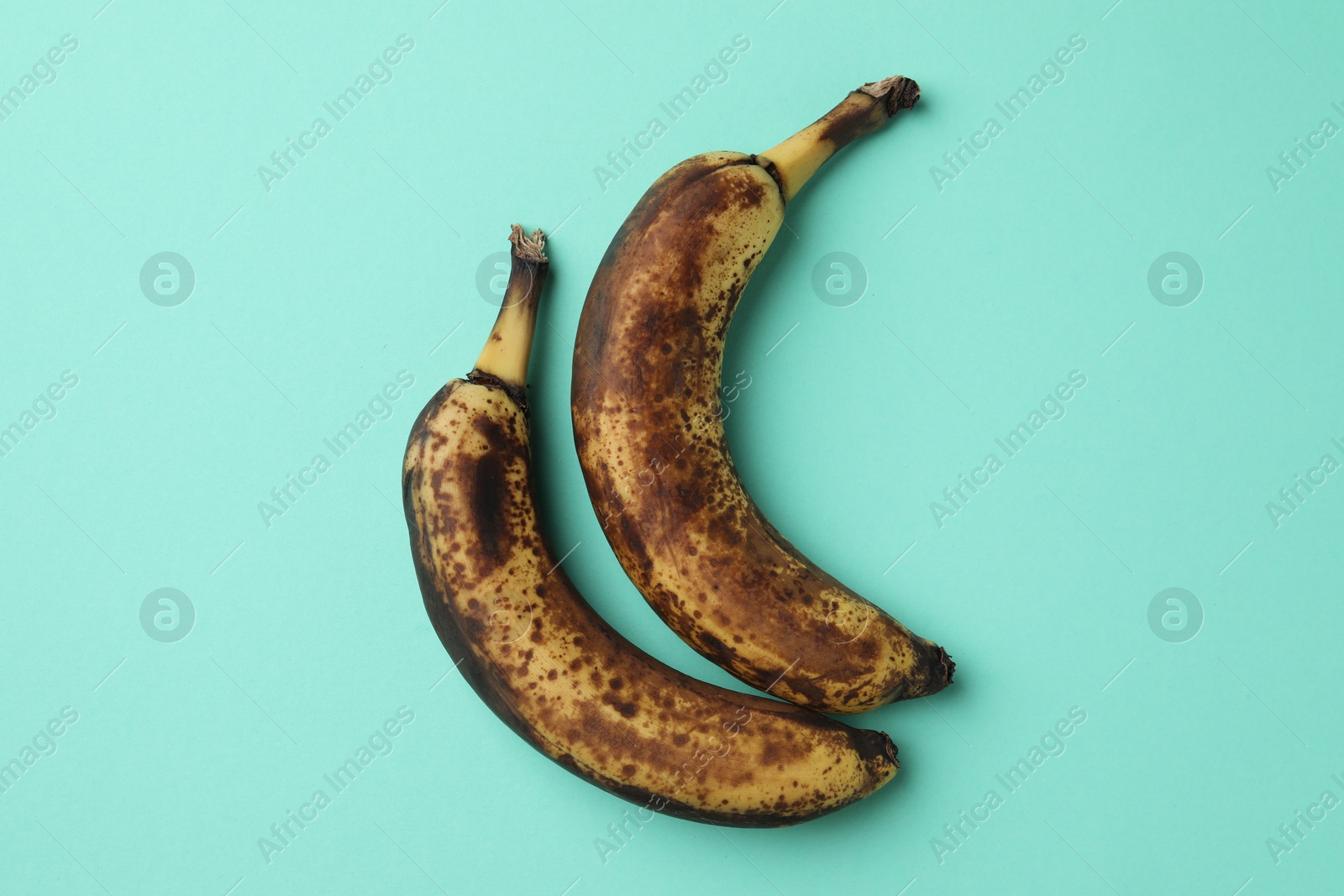 Photo of Overripe bananas with dark spots on turquoise background, top view