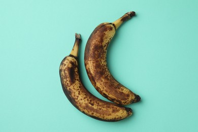 Overripe bananas with dark spots on turquoise background, top view