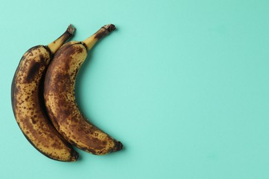 Overripe bananas with dark spots on turquoise background, top view. Space for text