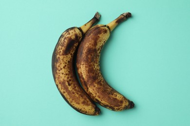 Overripe bananas with dark spots on turquoise background, top view