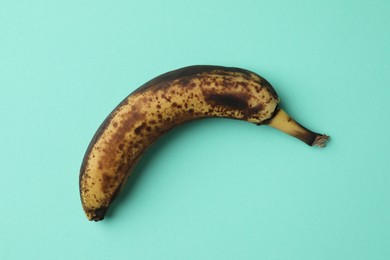 Photo of Overripe banana with dark spots on turquoise background, top view