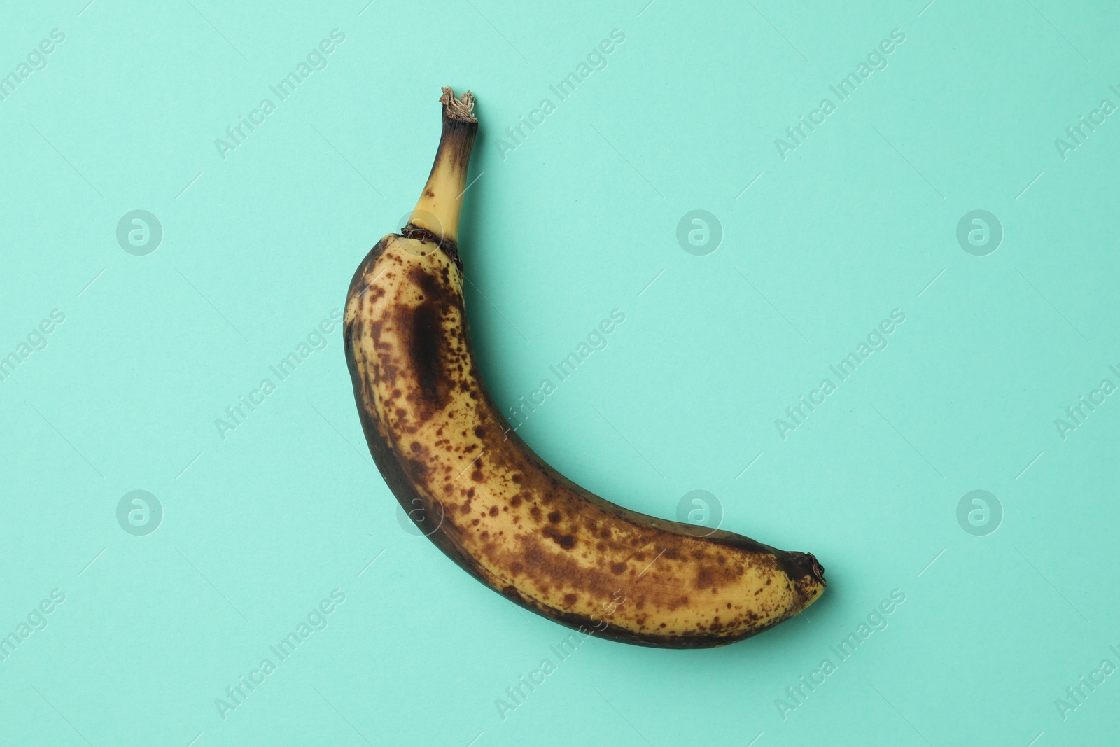 Photo of Overripe banana with dark spots on turquoise background, top view