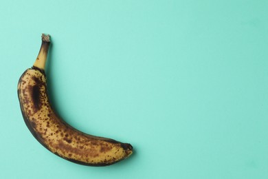 Photo of Overripe banana with dark spots on turquoise background, top view. Space for text