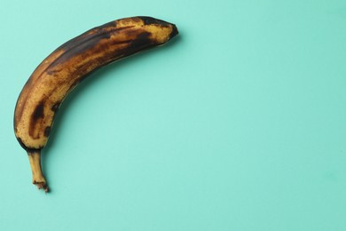 Photo of Overripe banana with dark spots on turquoise background, top view. Space for text